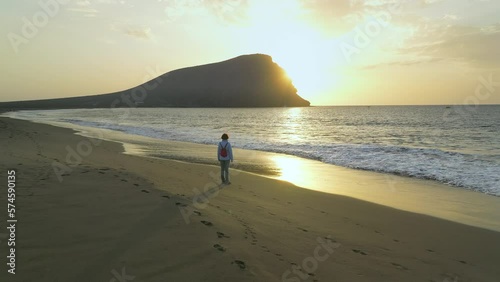 View of a hiker with backpack standing at La Tejita beach and looking to the volcanic cone of Montaña Roja during sunrise. Tenerife, (Canary Islands) photo