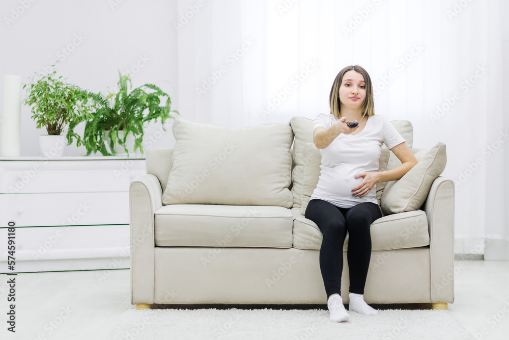 Pregnant woman facial expression sitting on sofa with remote control. Pregnant woman facial expression sitting on sofa with remote control.