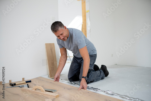 фотографія Middle aged man with grey hair and grey shirt laying parquet floor in new loft,