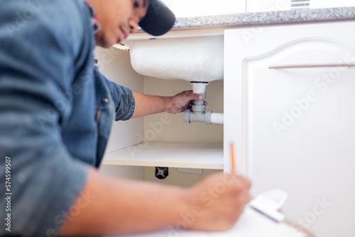 Plumber, checklist and pipe in home kitchen, workplace or industry for property development vision. Black man, construction worker and writing with notes, idea and paper for diy, interior and design