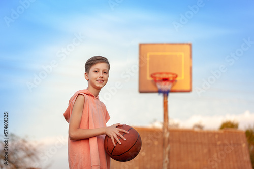 Kid boy playing basketball n sunset summer day in backyard. photo