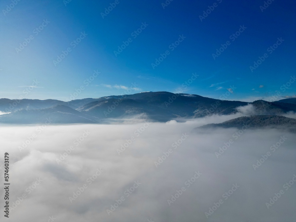 Panoramic aerial drone view on Grand Ballon Vosges mountains above the sea of clouds with a deep blue sky and a beautiful radiant sun, a fairy tale-like dreamy cotton bed at altitude