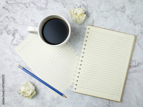 Coffee cup with notebook on marble texture background.