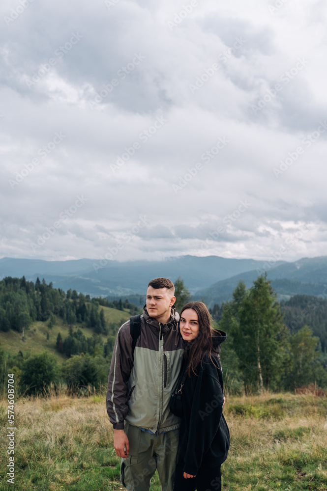 Photo of a beautiful young couple of tourists in the mountains against the background of beautiful views