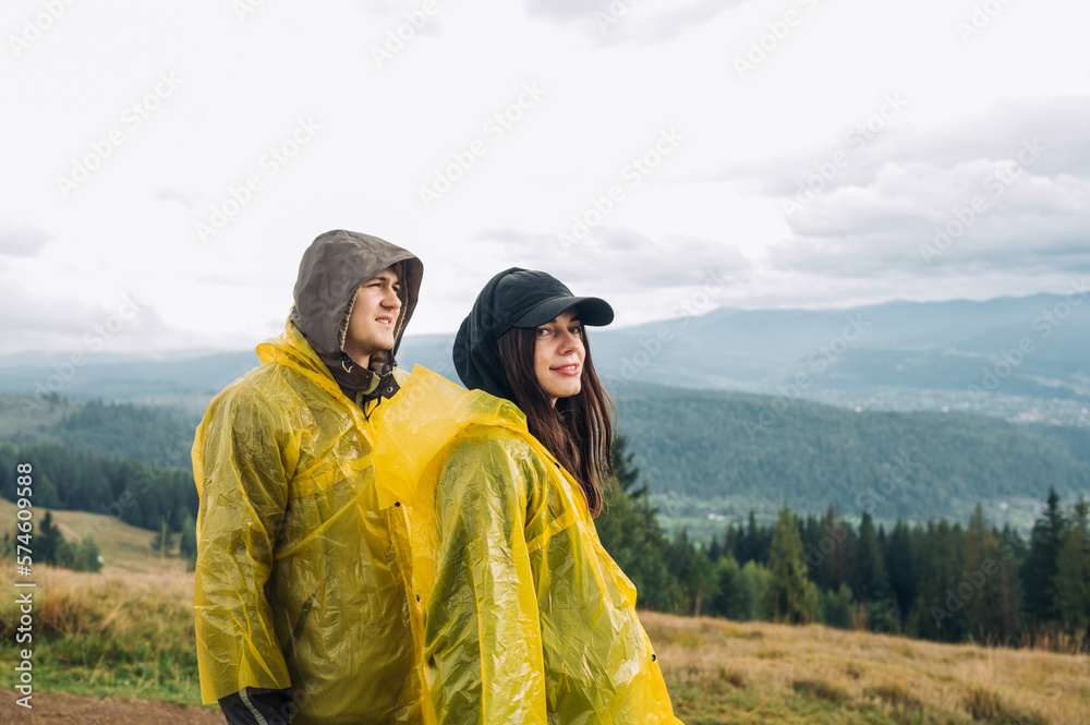 Photo of a beautiful couple of a man and a woman in raincoats in the mountains on the background of a beautiful landscape. Tourism concept.