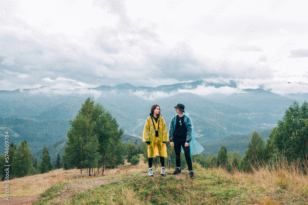A beautiful couple, a man and a woman, in raincoats on the top of a mountain on a hike against the background of beautiful views of the Carpathians.м
