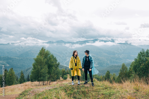 A beautiful couple, a man and a woman, in raincoats on the top of a mountain on a hike against the background of beautiful views of the Carpathians.м