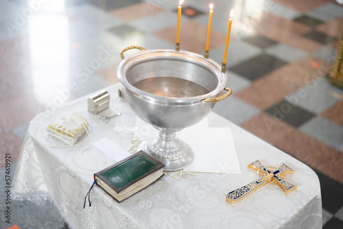 Baptismal font with wax candles and cross are on the table near Holy Bible. photo