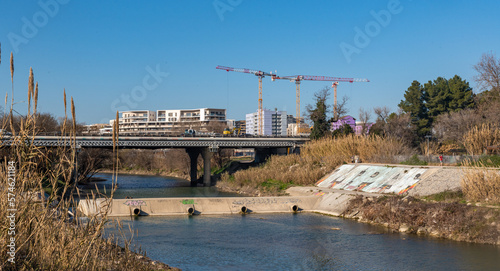 rives du Lez avec un pont  et une écluse avec des grues de construction au second plan et les immeubles de Port Marianne à Montpellier par une journée ensoleillée et un ciel bleu sans nuage.