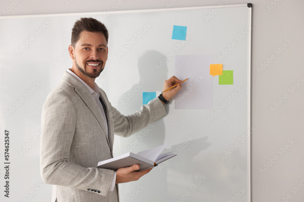 Happy teacher with book explaining something at whiteboard in classroom Happy teacher with book explaining something at whiteboard in classroom