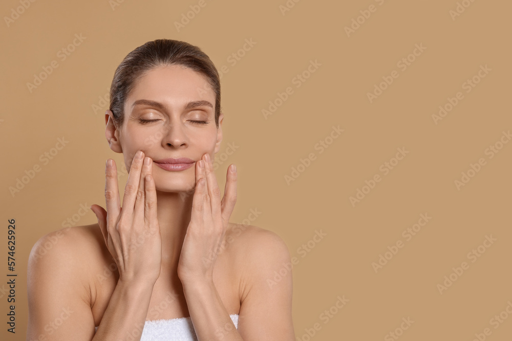 Woman massaging her face on beige background. Space for text Woman massaging her face on beige background. Space for text