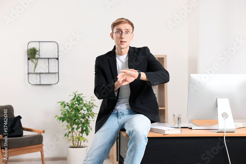 Emotional man checking time while sitting on table in office. Being late photo