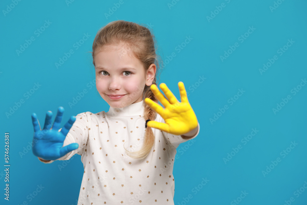 Little girl with hands painted in Ukrainian flag colors on light blue background, space for text. Love Ukraine concept Little girl with hands painted in Ukrainian flag colors on light blue background, space for text. Love Ukraine concept