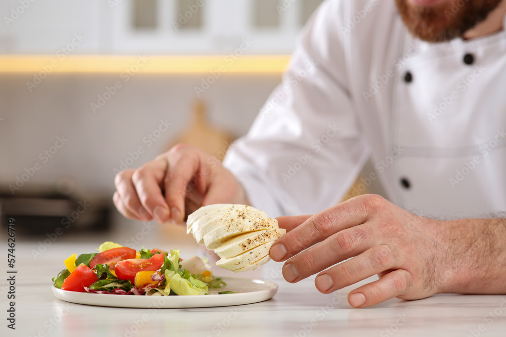 Closeup of professional chef adding mozzarella into delicious salad at marble table indoors, selective focus