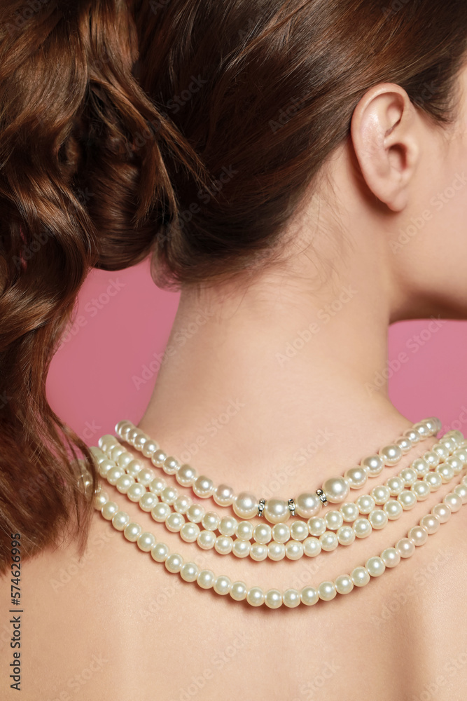 Young woman wearing elegant pearl necklace on pink background, back view