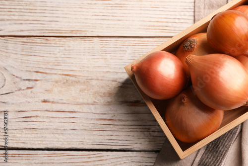 Crate with ripe onions on white wooden table, top view. Space for text