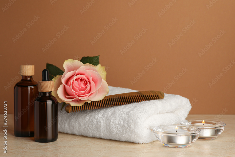 Composition with different spa products, beautiful flower and burning candles on beige table against brown background. Space for text
