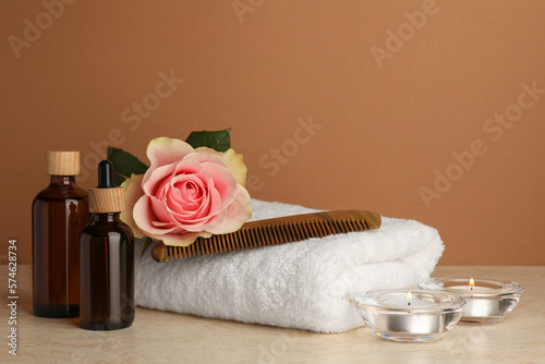 Composition with different spa products, beautiful flower and burning candles on beige table against brown background. Space for text