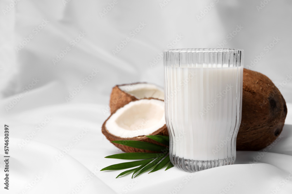 Glass of delicious coconut milk, palm leaves and coconuts on white fabric, space for text Glass of delicious coconut milk, palm leaves and coconuts on white fabric, space for text