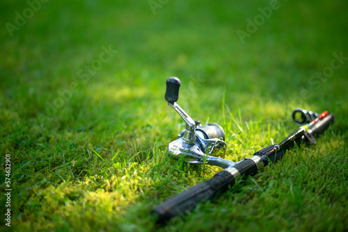 A telescopic fishing rod with a reel lies on the ground in the green grass. Fishing gear.
