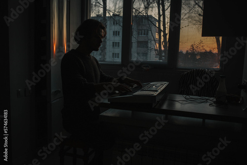 man at sunset in a dark room in the evening plays the piano alone.