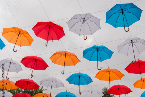 Low angle view: colorful umbrellas hanging against gray overcast sky and swaying in wind at summer city festival. Street decoration, celebration, art, holiday concept © zyabich