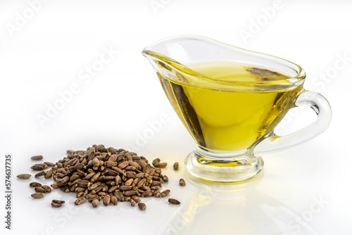Heap of milk thistle seeds and thistle oil in a glass gravy boat isolated on white background.