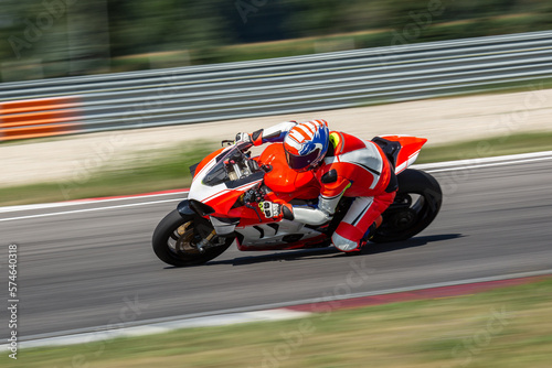 Murais de parede A motorcycle rider riding on an white,orange sport motorcycle through a corner at high speed