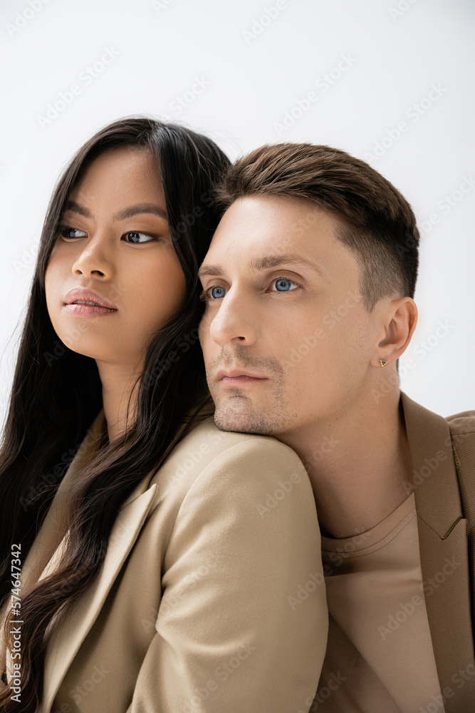 stylish man leaning on shoulder of brunette asian woman and looking away isolated on grey. stylish man leaning on shoulder of brunette asian woman and looking away isolated on grey.