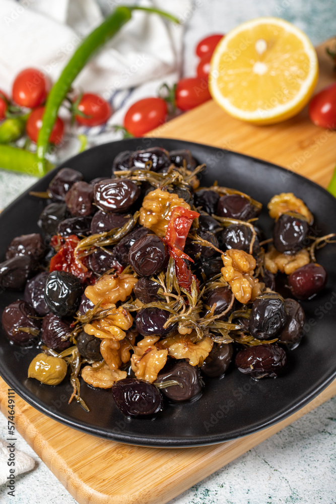 Mixed black olives. Special mixed olives prepared with dried red pepper, sun-dried tomatoes, thyme, walnuts and rosemary on a wooden serving plate. close up