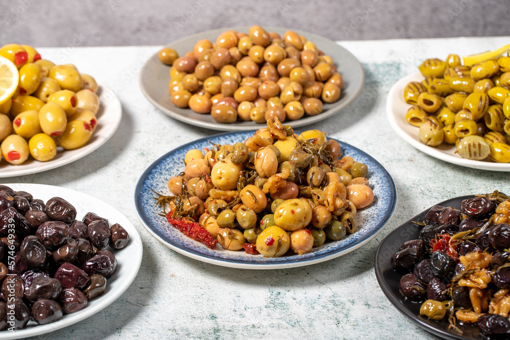 Olive varieties. Assortment of black and green olives on plate on gray background Olive varieties. Assortment of black and green olives on plate on gray background