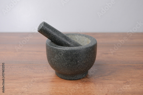 Black Stone granite mortar and pestle grinder on a wooden table with a grey background, 