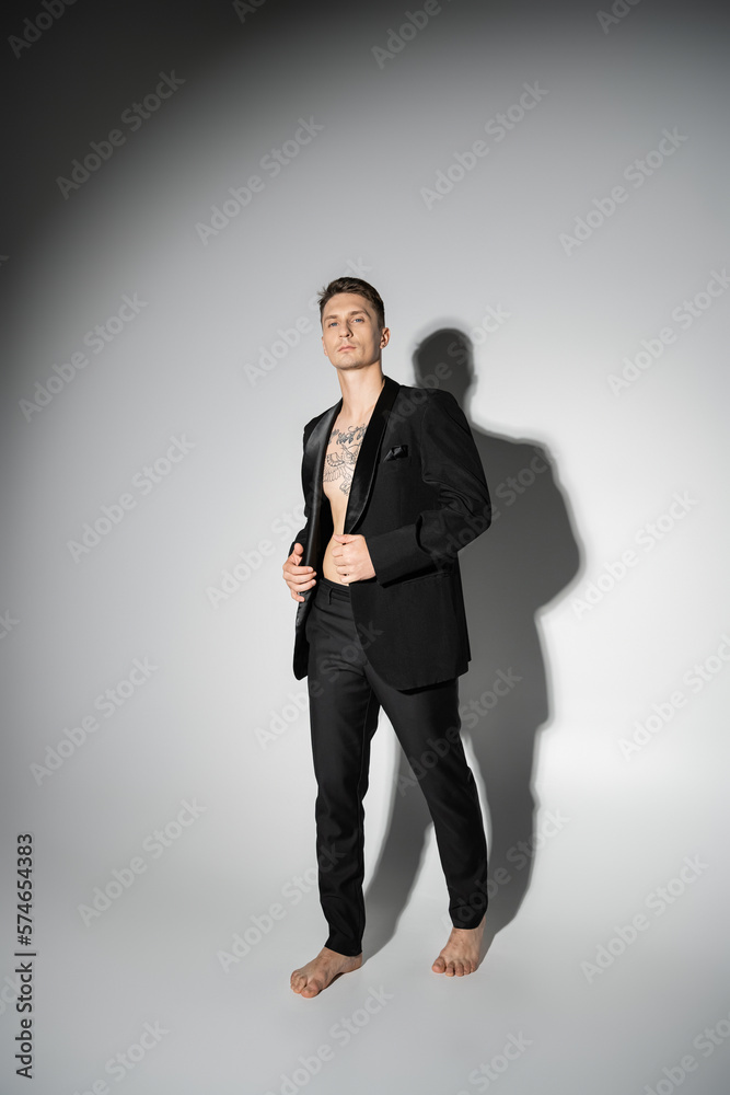 full length of barefoot man in black elegant suit standing on grey background with shadow. full length of barefoot man in black elegant suit standing on grey background with shadow.