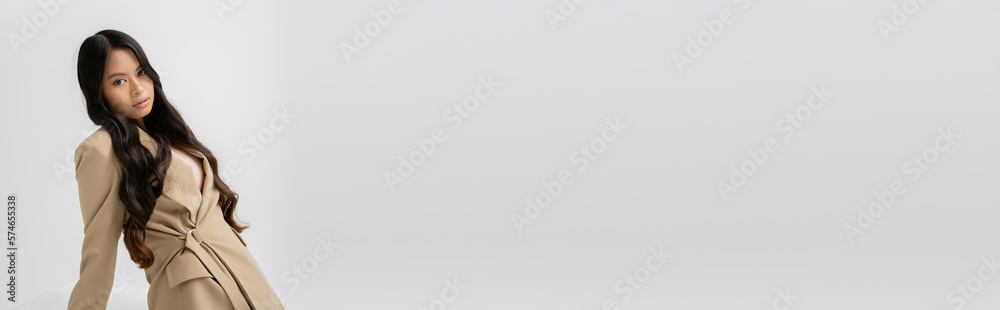 brunette asian woman in fashionable blazer looking at camera isolated on grey, banner. brunette asian woman in fashionable blazer looking at camera isolated on grey, banner.