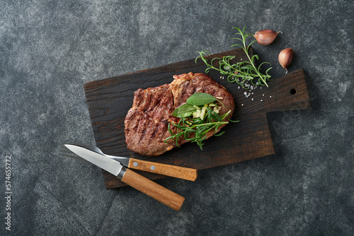 Steaks. Sliced grilled meat steak New York or Ribeye with spices rosemary and pepper on black marble board on old wooden background. Top view. Mock up.