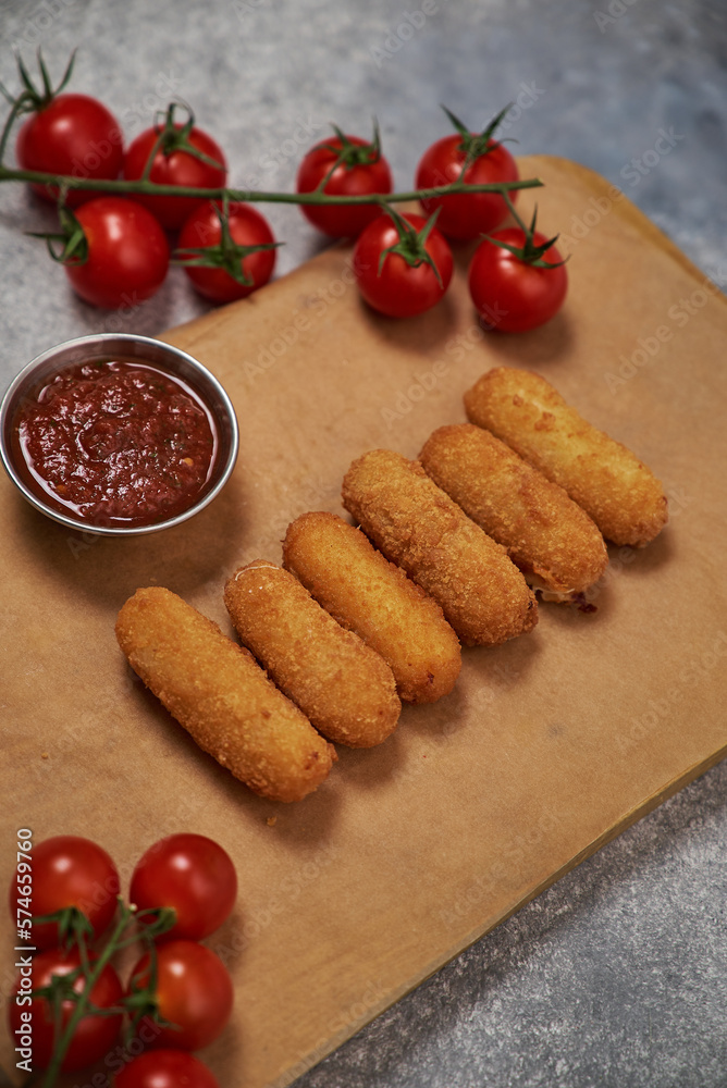 cheese sticks with breaded meat lie on a wooden board. with vegetables and decor around and sauce