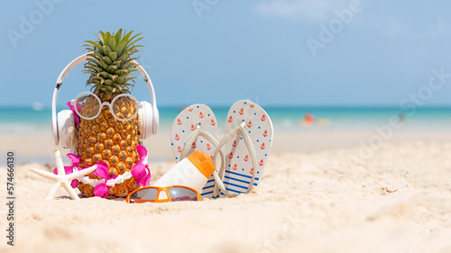 Fototapeta Naklejka Na Ścianę i Meble -  Summer in the party.  Hipster Pineapple Fashion in sunglass and listen music with sunblock and sandal on the sand beach beautiful blue sky background.  Fashion Summer Vacation