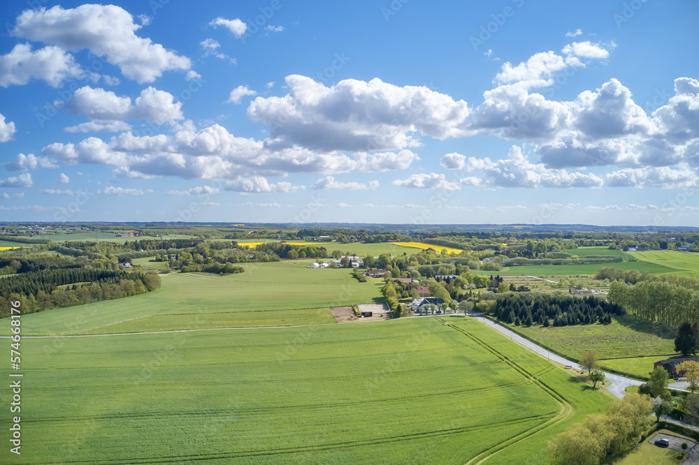 Drone view of farming and agricultural fields outdoors in Europe during summer or spring. Vibrant and bright pastures growing on endless farmland with blue sky background over a vast and open meadow