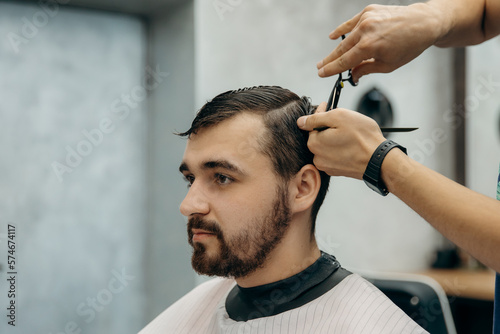 A professional hairdresser cuts a man with scissors in a barbershop. Men's beauty salon. Hair leveling.