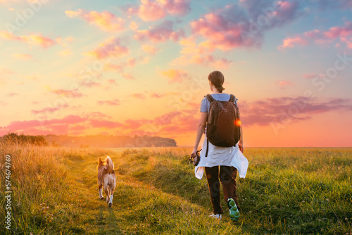 Young Woman Walking With Dog In Summer Meadow Grass During Sunset Sunrise Time. Healthy Lifestyle Walks Evening Summer Sunlight