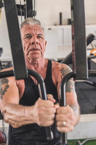 A rugged and tattooed older german man does a set of chest flyes on the pec deck machone. Working out pectoral muscles.