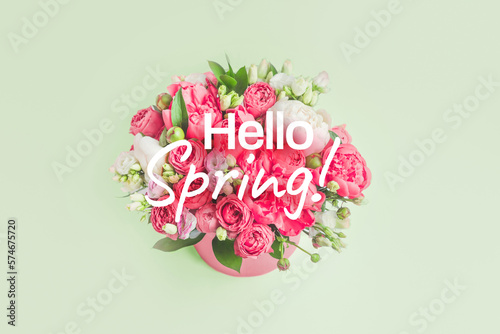 hello spring text with flowers. Bouquet of peonies, eustoma, rose in a pink box on green background