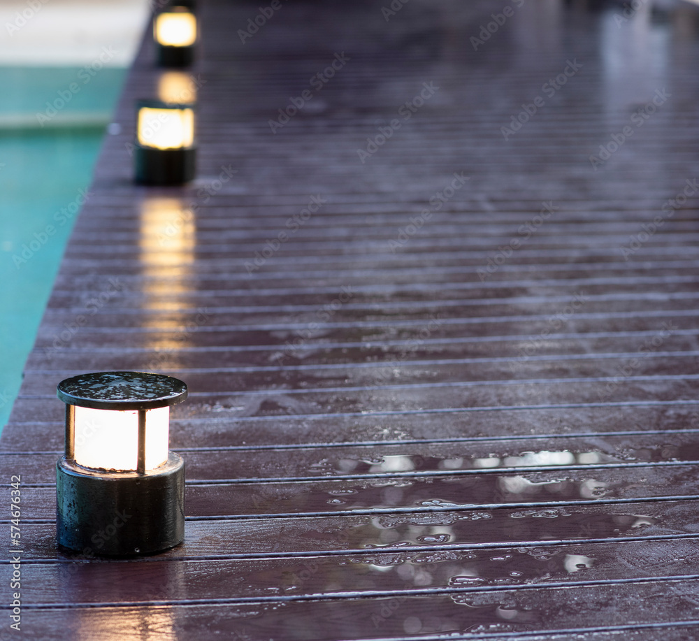 Close-up of a wooden walkway over water lit by spotlights at dusk. Selective focus Close-up of a wooden walkway over water lit by spotlights at dusk. Selective focus