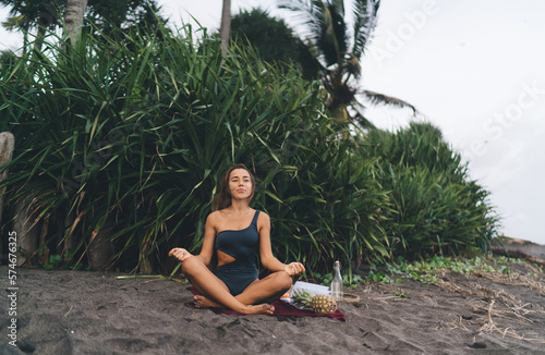 Relaxed woman in swimsuit meditating in lotus pose on beach
