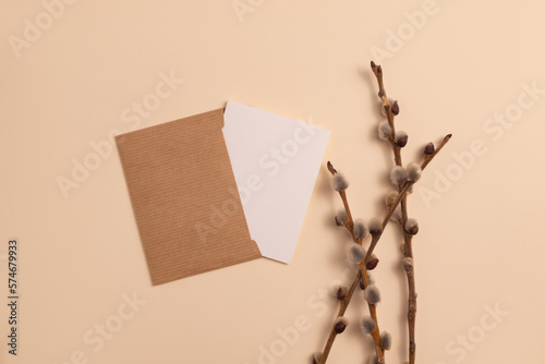 Mockup of an open invitation card made of eco-friendly kraft paper and decorated with a composition of dry flowering branches placed on a beige background