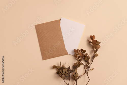 Mockup of an open invitation card made of ecological kraft paper and decorated with a composition of dried blueberry branches placed vertically on a beige background