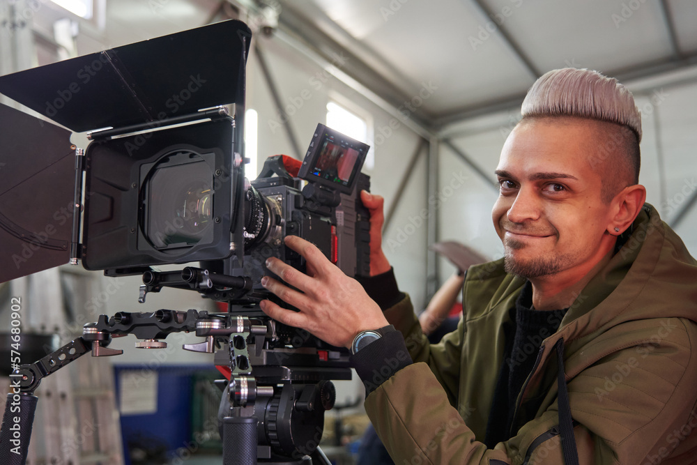 young caucasian man videographer smiling next to a professional movie camera young caucasian man videographer smiling next to a professional movie camera
