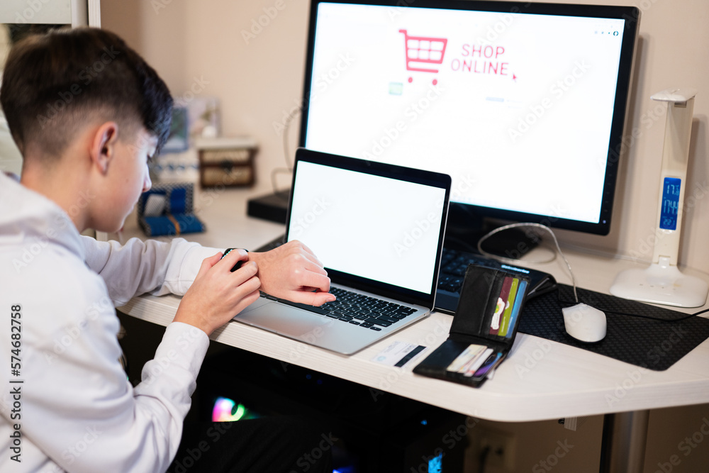 Happy teenage boy using laptop, smart watches and credit card, sitting at desk and ordering goods online from home. Happy teenage boy using laptop, smart watches and credit card, sitting at desk and ordering goods online from home.