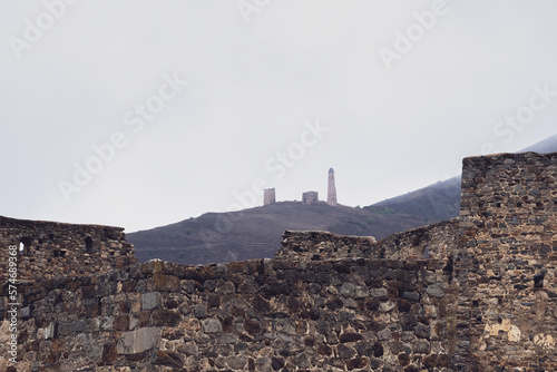 Old stone wall with arched passage. Misty morning in the Caucasus mountains. Medieval tower on foggy mountain slope background. Ingushetia region. photo