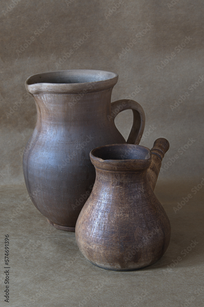 This charming image features a handmade clay coffee maker and a pitcher standing side by side on a brown paper background, softly illuminated by natural light.